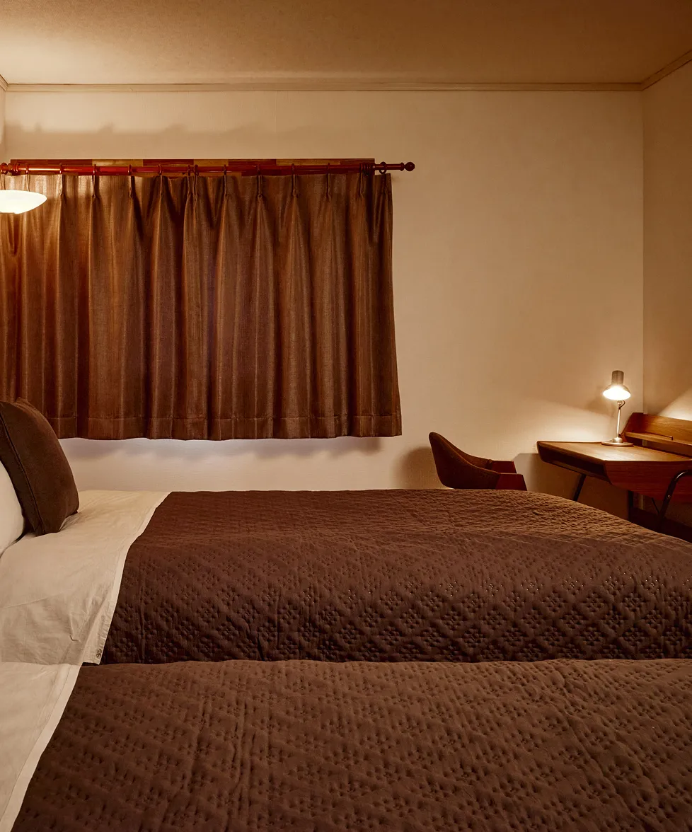 Beds beside a curtained window with a small bedside lamp