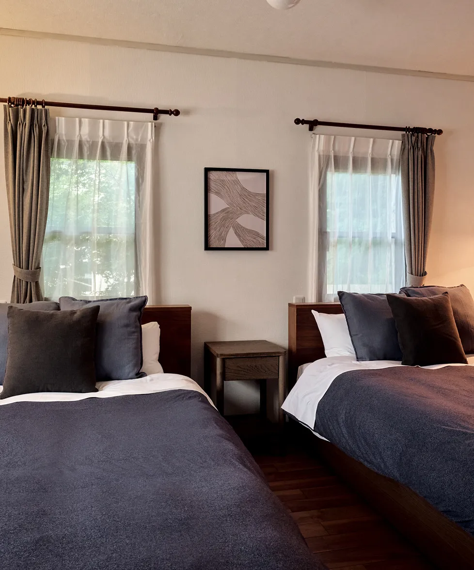 Bedroom with two beds in dark linen and lace-curtained windows