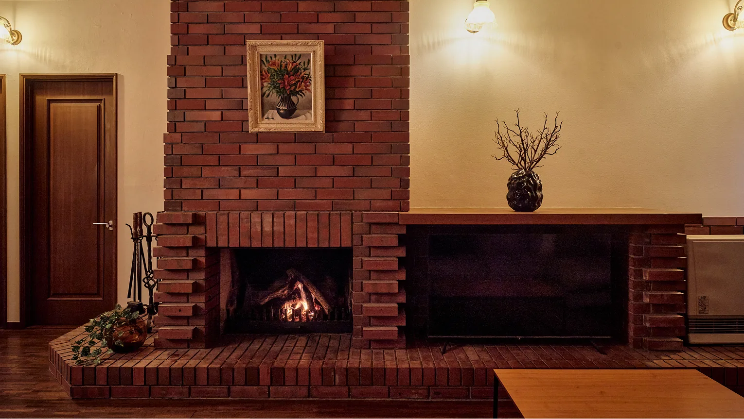 Corner of the living room with the fireplace lit and the wall lamps glowing