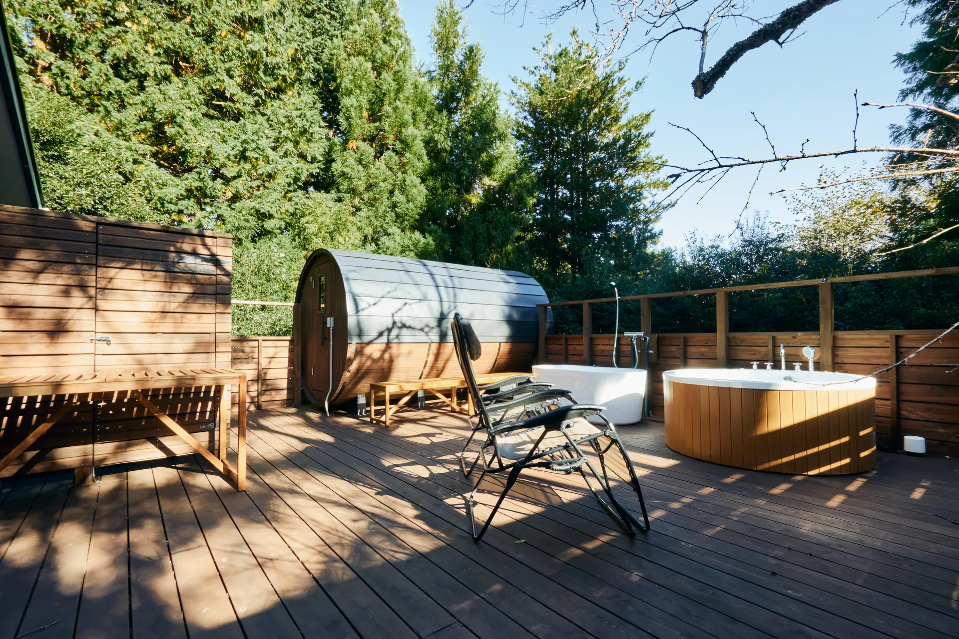 Barrel sauna and jacuzzi lined up on the sunlit wood deck
