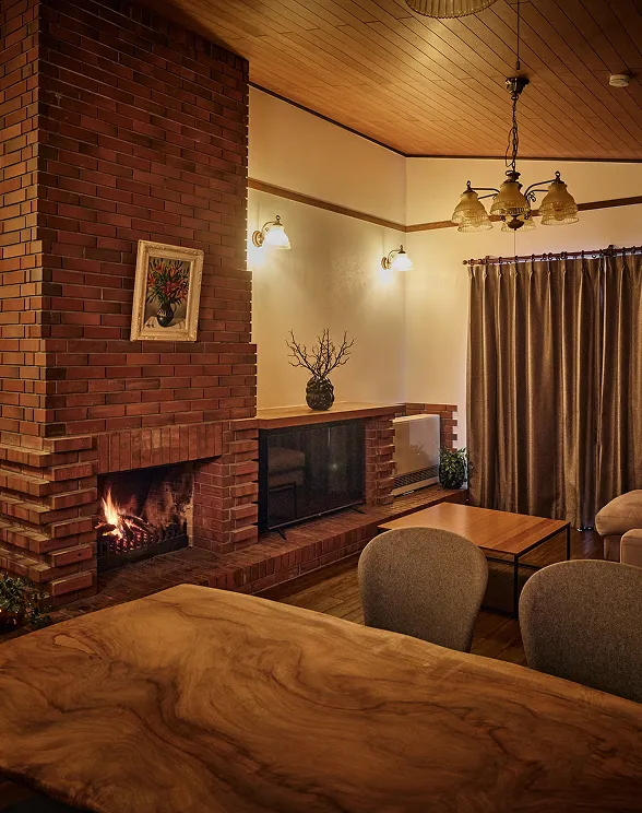 Living room with a fire burning in the brick fireplace, under a wood-paneled ceiling