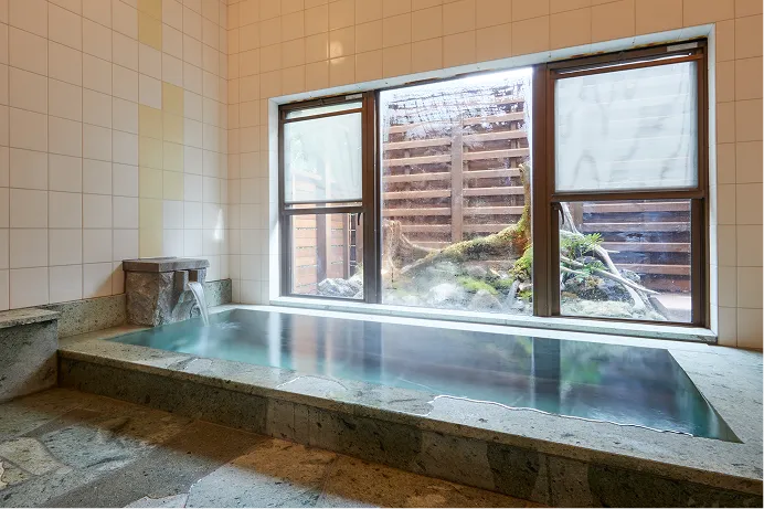 Towada stone bathtub filled with hot spring water beside a garden window
