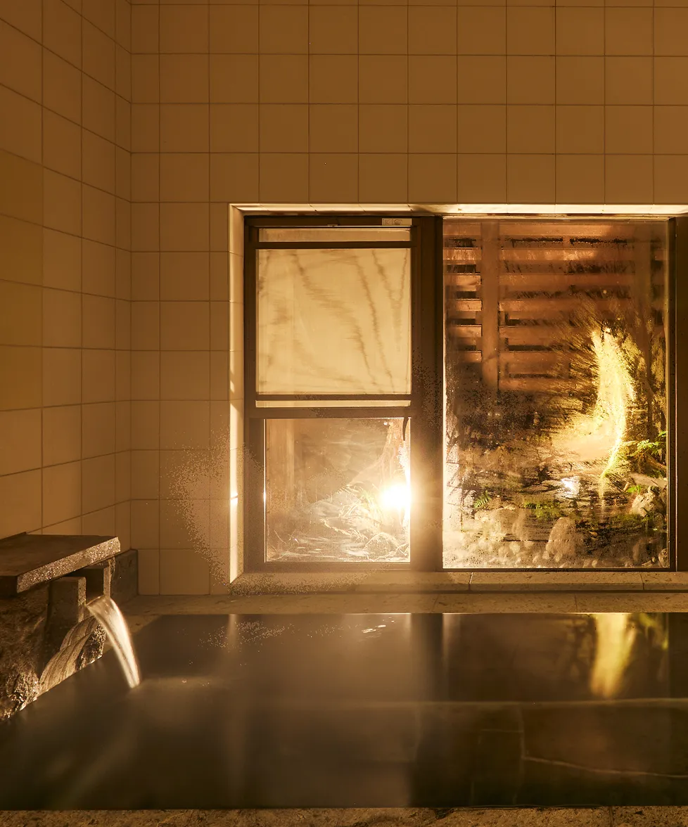 The stone bath at night, lit warmly as water pours from the spout