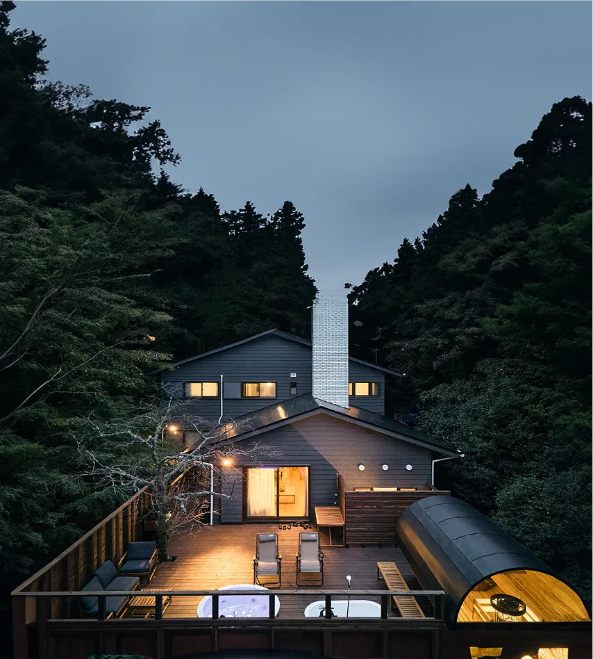 The villa at dusk, half-hidden among the trees, with its deck lit