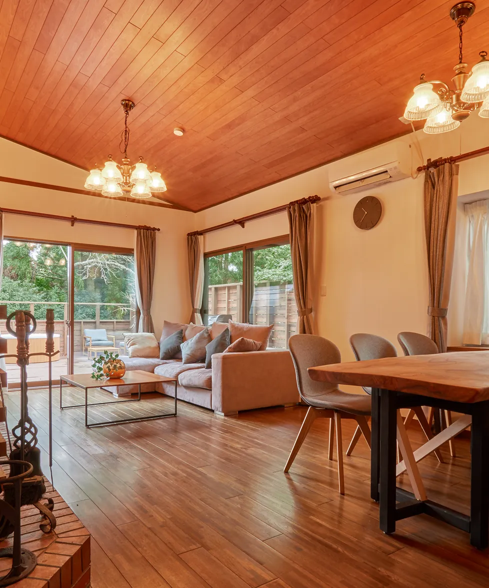 Sofas and dining table beneath the chandelier, with windows to the forest
