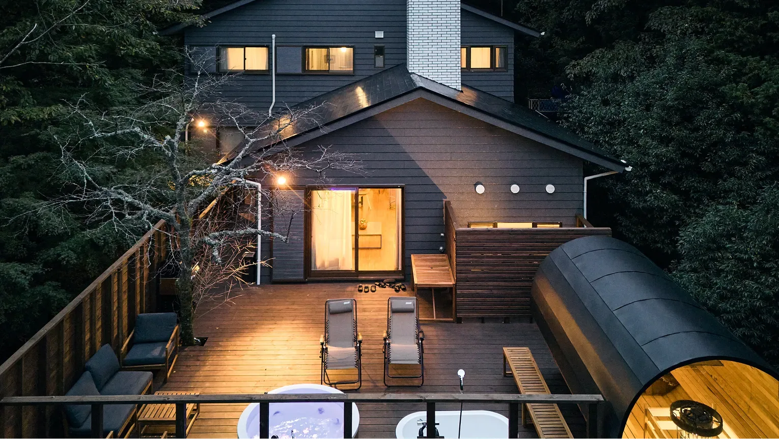 Navy timber lodge at dusk, its lit windows and wooden deck glowing among the trees