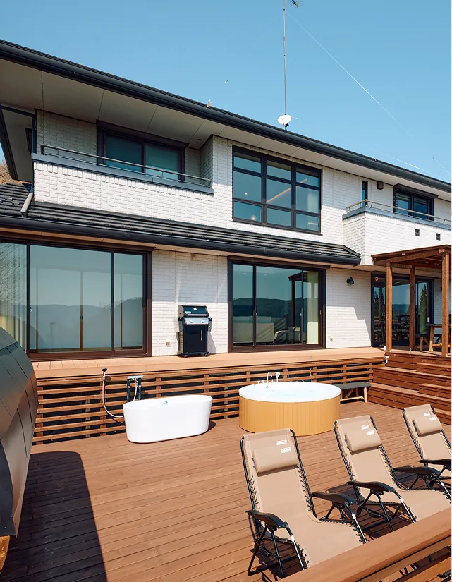 White brick facade of the villa with bathtub, jacuzzi, and loungers on the wooden deck