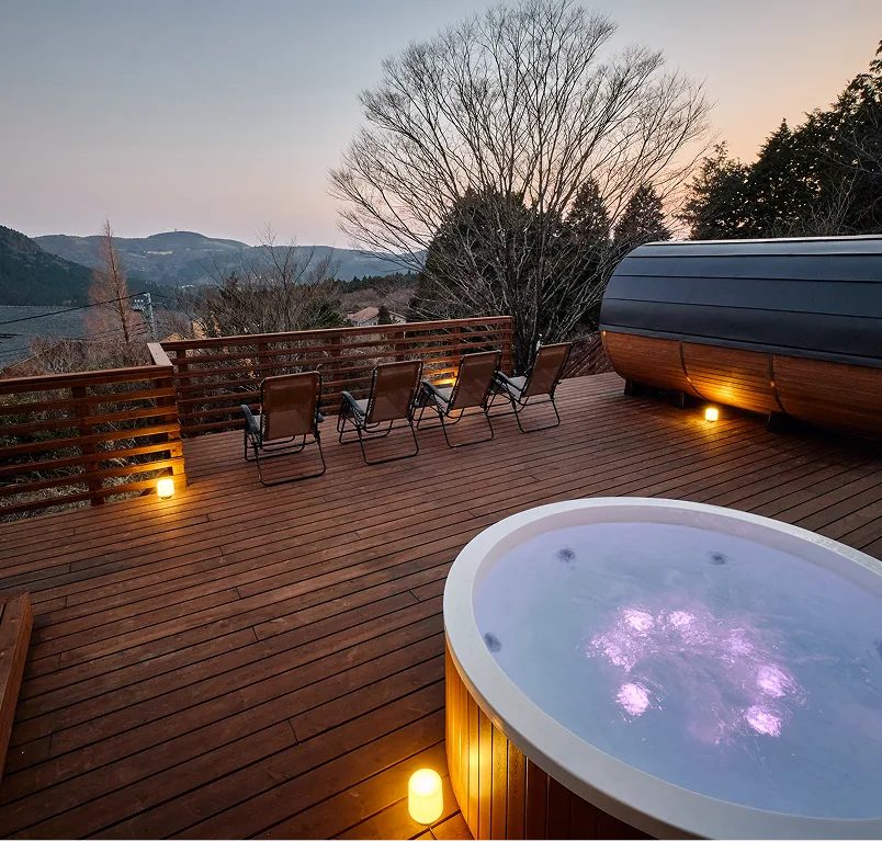 Lit jacuzzi and barrel sauna on the deck at dusk