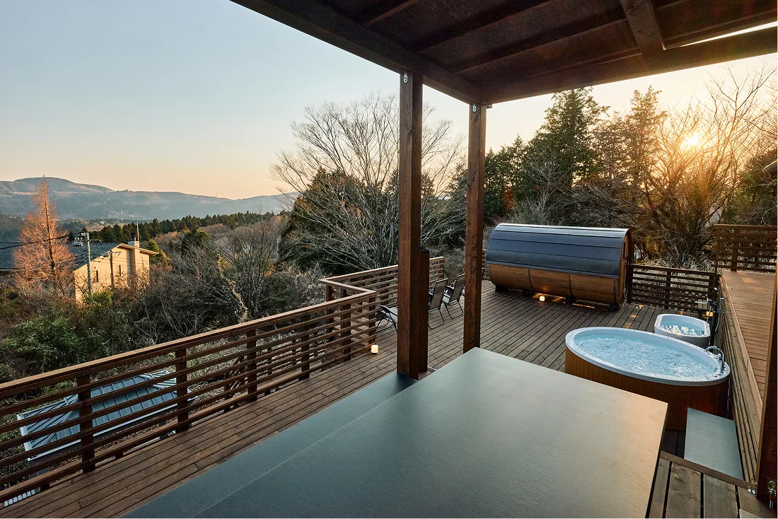 Evening wooden deck with jacuzzi and barrel sauna seen from the covered terrace
