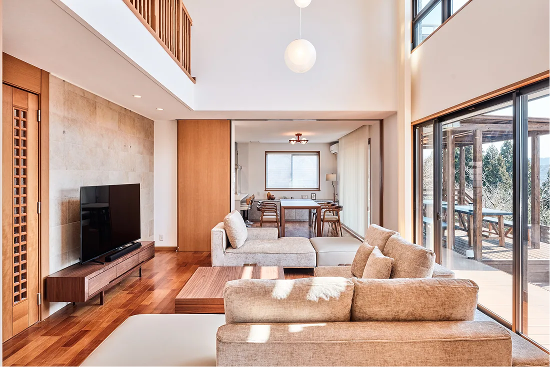 Living room with a large TV, sofas, and wide openings to the deck
