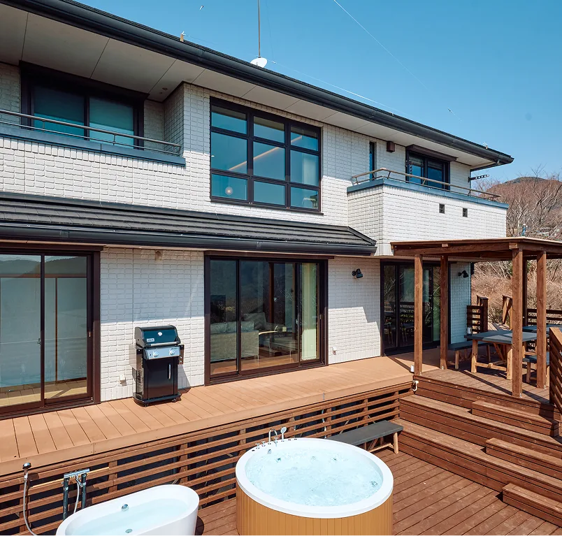 BBQ grill on the wooden deck in front of the white brick villa, with jacuzzi and bathtub